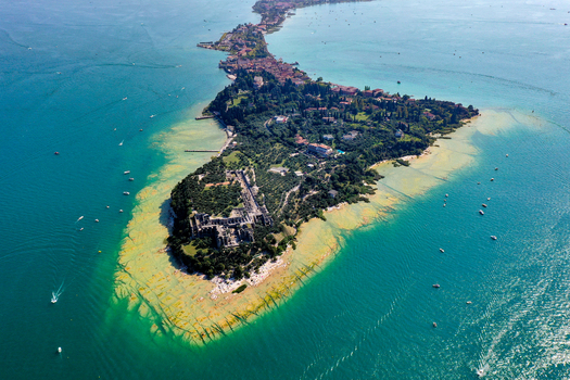 Aerial view of the turquoise waters of Jamaica Beach and the historic Grotte di Catullo ruins on the tip of the Sirmione peninsula at Lake Garda Sirmione Lombardia Italy.