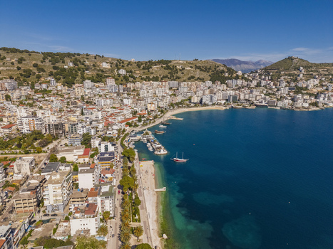 Aerial view of the coastal city of Saranda with its urban buildings sandy beach and boats docked in the Ionian Sea in Saranda Vlore County Albania. Aerial view of the coastal city of Saranda with its urban buildings sandy beach and boats docked in the Ionian Sea in Saranda Vlore County Albania.