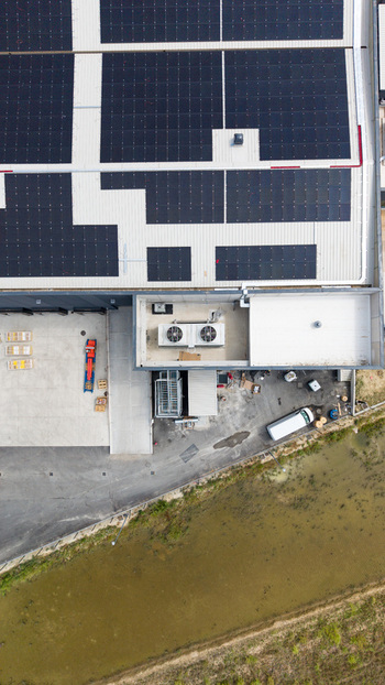 Aerial view of a modern logistics warehouse for fresh produce featuring extensive rooftop solar panels industrial cooling systems and a loading dock in Melegnano Lombardy Italy.