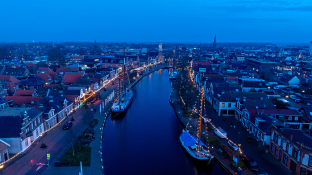 Aerial view of the canal in Lemmer at twilight featuring historic buildings traditional sailing ships and festive string lights along the waterfront. Lemmer Friesland Netherlands. Aerial view of the canal in Lemmer at twilight featuring historic buildings traditional sailing ships and festive string lights along the waterfront. Lemmer Friesland Netherlands.