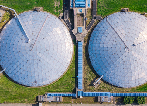Aerial view of a waste water treatment plant featuring two large circular tanks with geodesic dome covers surrounded by green grass and industrial infrastructure in Poland. Aerial view of a waste water treatment plant featuring two large circular tanks with geodesic dome covers surrounded by green grass and industrial infrastructure in Poland.