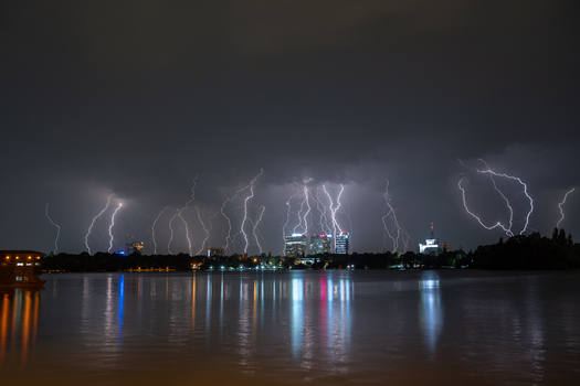 View of multiple lightning bolts striking the night sky over the illuminated Bucharest skyline reflected in the calm waters of Herastrau Lake Bucharest Bucharest Romania. View of multiple lightning bolts striking the night sky over the illuminated Bucharest skyline reflected in the calm waters of Herastrau Lake Bucharest Bucharest Romania.