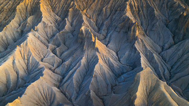 Aerial view of the eroded badlands landscape with sharp ridges and deep shadows cast by the golden hour light in Hanksville Utah United States.
