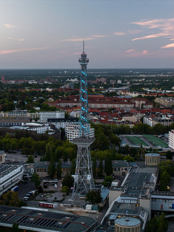 Aerial view of the iconic Funkturm Berlin radio tower illuminated with blue lights surrounded by the Messe Berlin exhibition grounds and urban cityscape in Berlin Berlin Germany. Aerial view of the iconic Funkturm Berlin radio tower illuminated with blue lights surrounded by the Messe Berlin exhibition grounds and urban cityscape in Berlin Berlin Germany.