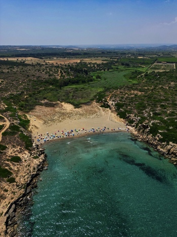 Aerial view of Calamosche Beach with turquoise water sandy shore and colorful umbrellas nestled between rocky cliffs Noto Sicilia Italy.