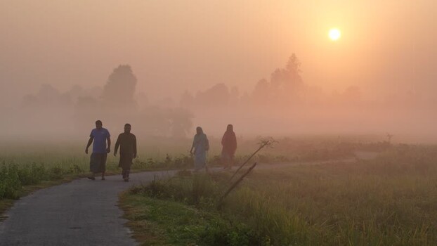 View of people walking on a foggy rural road at sunrise Bangladesh.