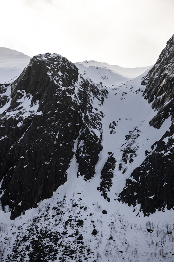 View of snow covered mountain peaks and dark rocky cliffs under an overcast winter sky Kvaloya Troms Norway. View of snow covered mountain peaks and dark rocky cliffs under an overcast winter sky Kvaloya Troms Norway.
