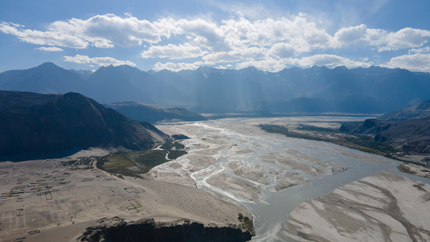 Aerial view of the expansive Shigar Valley with its braided river channels surrounding rugged mountain ranges and clear blue sky in Shigar Gilgit Pakistan.