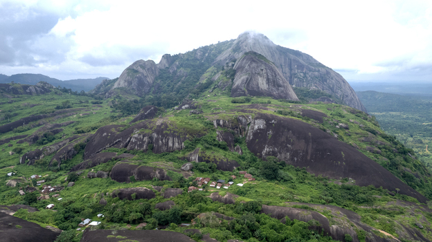 Aerial view of Idanre Hill featuring massive granite rock formations lush green vegetation and small village dwellings nestled among the slopes in Idanre Ondo State Nigeria. Aerial view of Idanre Hill featuring massive granite rock formations lush green vegetation and small village dwellings nestled among the slopes in Idanre Ondo State Nigeria.