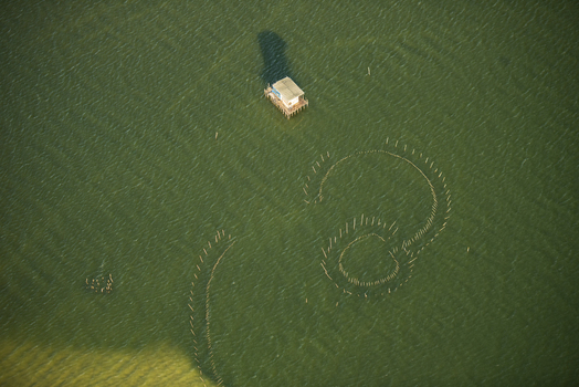 Aerial view of a small stilt house and circular fishing stakes in the calm green waters of the bay in Rio de Janeiro Rio de Janeiro Brazil. Aerial view of a small stilt house and circular fishing stakes in the calm green waters of the bay in Rio de Janeiro Rio de Janeiro Brazil.