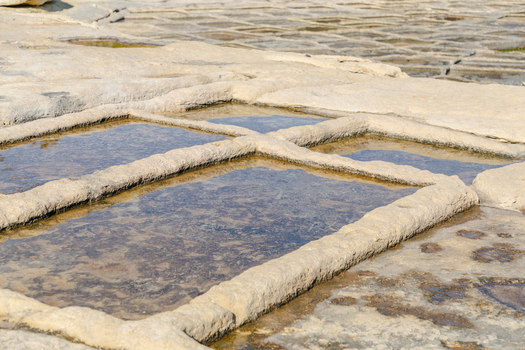View of geometric salt pans filled with shallow water reflecting the sky carved into the rugged coastline under the sun Marsaskala Malta. View of geometric salt pans filled with shallow water reflecting the sky carved into the rugged coastline under the sun Marsaskala Malta.