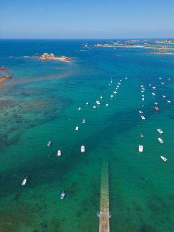 Aerial view of Plage de Port Blanc with numerous white boats anchored in turquoise waters near a stone pier and rocky islands in Penvenan Bretagne France. Aerial view of Plage de Port Blanc with numerous white boats anchored in turquoise waters near a stone pier and rocky islands in Penvenan Bretagne France.