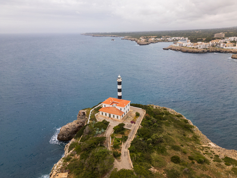 Aerial view of the Far de Portocolom lighthouse on a rocky cliff overlooking the Mediterranean Sea in Portocolom Balearic Islands Spain. Aerial view of the Far de Portocolom lighthouse on a rocky cliff overlooking the Mediterranean Sea in Portocolom Balearic Islands Spain.