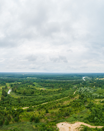 Aerial view of a lush green landscape with dense forests a winding river and dirt paths under a cloudy sky in Latvia. Aerial view of a lush green landscape with dense forests a winding river and dirt paths under a cloudy sky in Latvia.
