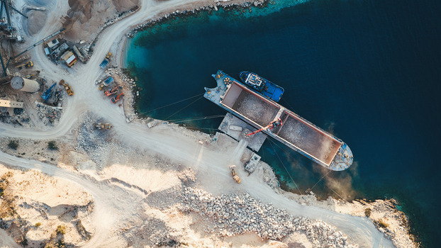 Aerial view of a cargo ship being loaded with white stone at the Jadrankamen quarry with heavy machinery and deep blue water in Pucisca Splitsko dalmatinska Croatia. Aerial view of a cargo ship being loaded with white stone at the Jadrankamen quarry with heavy machinery and deep blue water in Pucisca Splitsko dalmatinska Croatia.