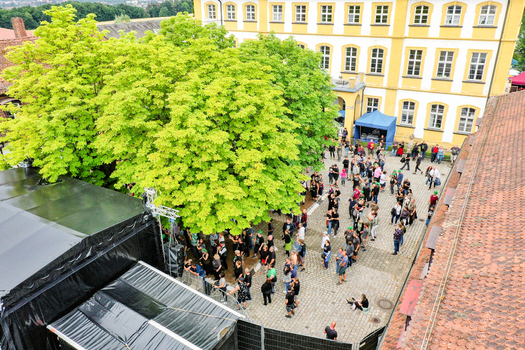Aerial view of Schloss Jagersburg with a crowd of people gathered in the courtyard next to lush green trees and a yellow historic building in Eggolsheim Bayern Germany. Aerial view of Schloss Jagersburg with a crowd of people gathered in the courtyard next to lush green trees and a yellow historic building in Eggolsheim Bayern Germany.