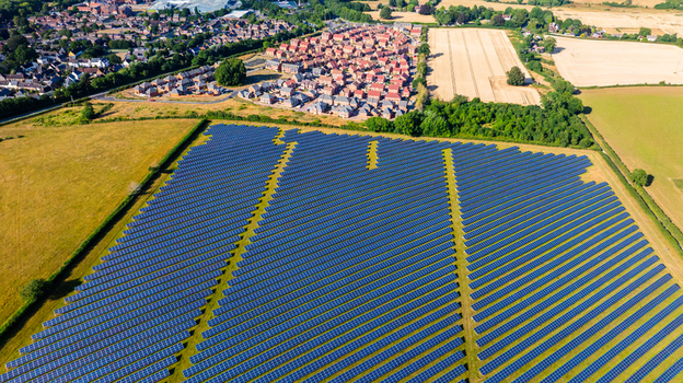 Aerial view of a large solar farm with rows of photovoltaic panels situated next to a residential neighborhood and agricultural fields in Dorset England United Kingdom. Aerial view of a large solar farm with rows of photovoltaic panels situated next to a residential neighborhood and agricultural fields in Dorset England United Kingdom.