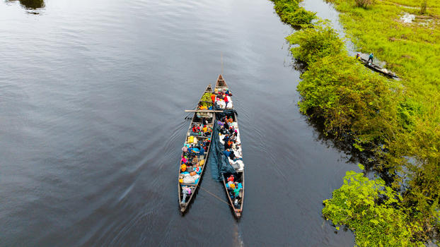 Aerial view of two long wooden canoes filled with passengers and goods navigating the river near lush green banks in Itu Akwa Ibom Nigeria. Aerial view of two long wooden canoes filled with passengers and goods navigating the river near lush green banks in Itu Akwa Ibom Nigeria.