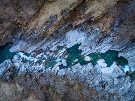 Aerial view of the emerald green waters of the Verzasca river flowing through steep granite rock formations and rugged terrain in Valle Verzasca Verzasca Ticino Switzerland. Aerial view of the emerald green waters of the Verzasca river flowing through steep granite rock formations and rugged terrain in Valle Verzasca Verzasca Ticino Switzerland.