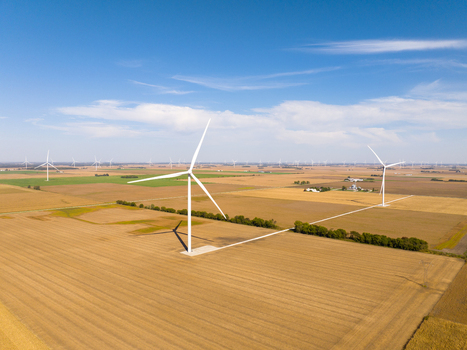Aerial view of wind turbines standing in vast golden agricultural fields under a clear blue sky in Wolcott Indiana United States.