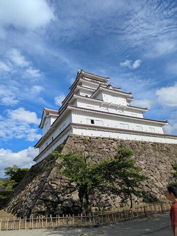 View of Tsuruga Castle with its white walls and tiered roof rising above a massive stone foundation in Aizuwakamatsu Fukushima Japan.