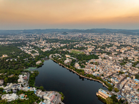 Aerial view of Udaipur featuring the expansive Fateh Sagar Lake surrounding architecture lush trees and distant hills under a warm sunset sky. Udaipur Rajasthan India.