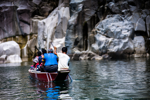 Meghalaya India 31 March 2023 View of people in a wooden boat navigating the clear waters of the Umngot River surrounded by towering rocky cliffs. Meghalaya India 31 March 2023 View of people in a wooden boat navigating the clear waters of the Umngot River surrounded by towering rocky cliffs.