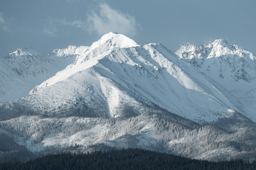 View of snow capped mountain peaks of the Tatra Mountains rising above a dense evergreen forest under a clear sky in Czarna Gora Lesser Poland Voivodeship Poland. View of snow capped mountain peaks of the Tatra Mountains rising above a dense evergreen forest under a clear sky in Czarna Gora Lesser Poland Voivodeship Poland.