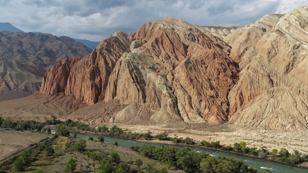 Aerial view of the rugged multi colored mountain range rising above a winding river flowing through the valley in Naryn Region Kyrgyzstan. Aerial view of the rugged multi colored mountain range rising above a winding river flowing through the valley in Naryn Region Kyrgyzstan.