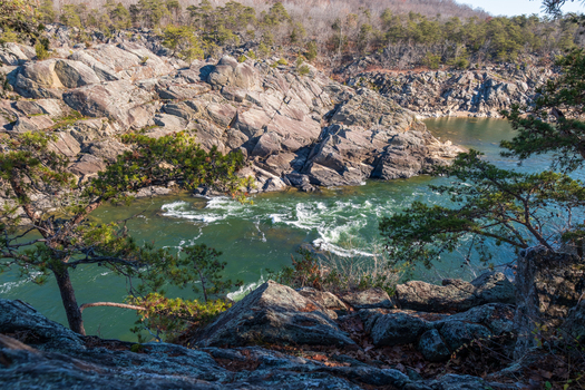 View of the rushing water swirling through the rocky gorge framed by trees and boulders under a clear sky Great Falls National Park Virginia United States. View of the rushing water swirling through the rocky gorge framed by trees and boulders under a clear sky Great Falls National Park Virginia United States.