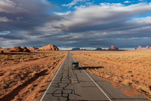 View of a car driving along a long straight road through the iconic red rock landscape of Monument Valley Tribal Park in Oljato Monument Valley Utah United States.