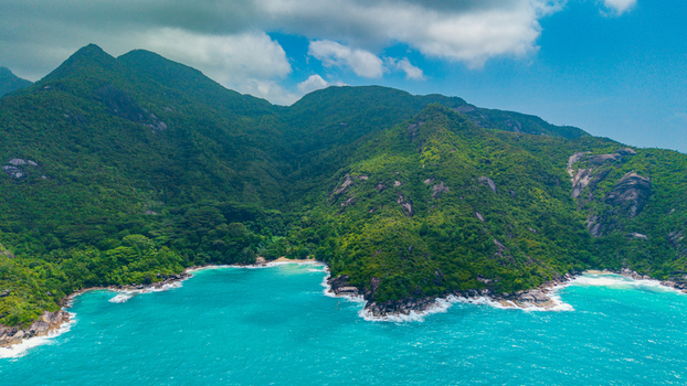 Aerial view of Anse Soleil Beachcomber Hotel nestled between lush green mountains and turquoise waters in Mahe Baie Lazare Seychelles.