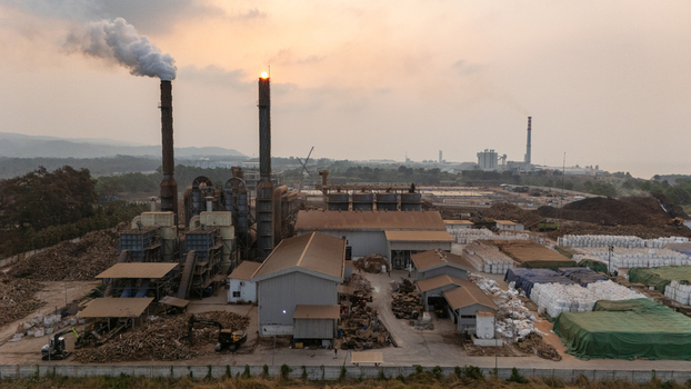 Aerial view of Kawasan Industri Terpadu Batang with industrial smoke stacks storage facilities and biomass piles under a golden sunset in Kecamatan Gringsing Jawa Tengah Indonesia.