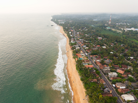 Aerial view of the tropical coastline with sandy beaches turquoise ocean waves and lush green palm trees along the coastal road in Galle Southern Province Sri Lanka.