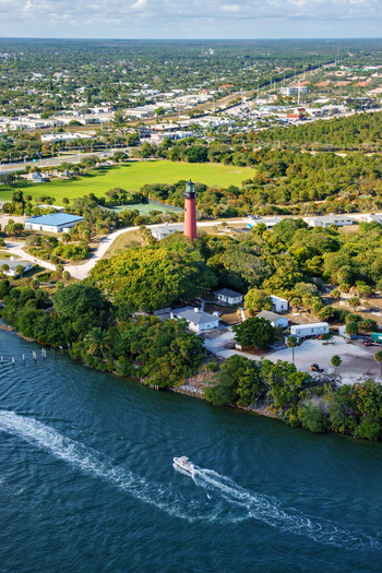 Aerial view of the Jupiter Inlet Lighthouse dramatically piercing the skyline amidst lush greenery with the Intracoastal Waterway reflecting the sky s azure hues Jupiter Florida United States.