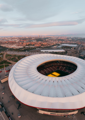 Aerial view of Riyadh Air Metropolitano Stadium with its distinctive white roof and illuminated pitch surrounded by the urban landscape of Madrid Comunidad de Madrid Spain.
