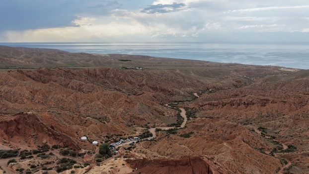 Aerial view of the red sandstone rock formations of Jety Oguz Canyon with a winding path parked vehicles and the distant Issyk Kul lake in Jety Oguz Issyk Kul Region Kyrgyzstan. Aerial view of the red sandstone rock formations of Jety Oguz Canyon with a winding path parked vehicles and the distant Issyk Kul lake in Jety Oguz Issyk Kul Region Kyrgyzstan.
