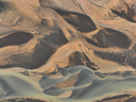 Aerial view of the volcanic landscape featuring dark basaltic sand braided river channels and textured terrain in Selfoss Sveitarfelagid Arborg Iceland. Aerial view of the volcanic landscape featuring dark basaltic sand braided river channels and textured terrain in Selfoss Sveitarfelagid Arborg Iceland.