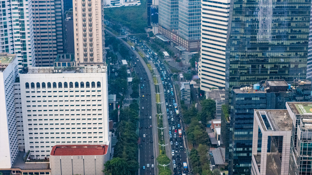 Aerial view of the dense urban skyline with heavy traffic flowing along a major road surrounded by modern skyscrapers and office buildings in Jakarta Indonesia.