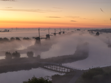 Aerial view of Unesco World Heritage Kinderdijk windmills shrouded in thick morning mist during a golden sunrise Kinderdijk Zuid Holland Netherlands.