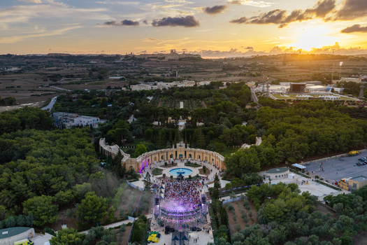 Attard Northern Region Malta 20 September 2026 Aerial view of Park Nazzjonali Ta Qali featuring an outdoor concert stage with crowds gathered at sunset surrounded by lush parkland. Attard Northern Region Malta 20 September 2026 Aerial view of Park Nazzjonali Ta Qali featuring an outdoor concert stage with crowds gathered at sunset surrounded by lush parkland.