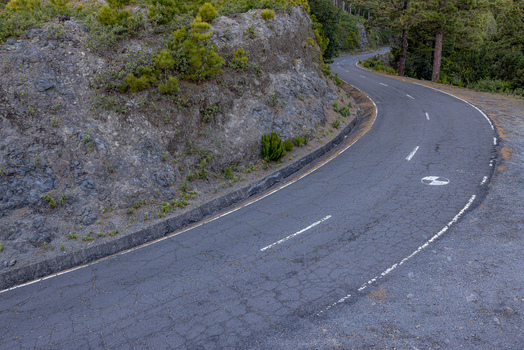 View of a winding asphalt road curving through the volcanic landscape of Caldera de Taburiente National Park with rocky slopes and pine trees El Paso Canarias Spain. View of a winding asphalt road curving through the volcanic landscape of Caldera de Taburiente National Park with rocky slopes and pine trees El Paso Canarias Spain.