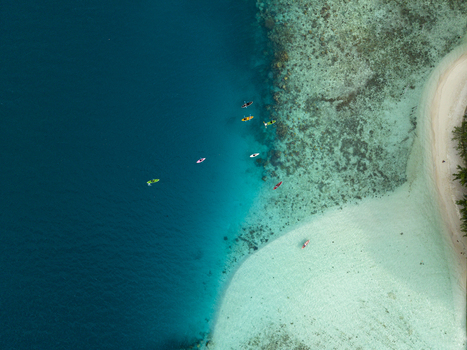 Aerial view of a serene island with a pristine white beach meeting the clear turquoise waters with kayaks dotting the tranquil sea Menjangan Kecil Karimunjawa Indonesia.