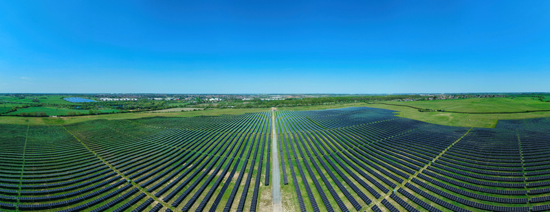 Aerial view of a large solar farm with rows of photovoltaic panels stretching across green fields under a clear blue sky in Little Irchester England United Kingdom. Aerial view of a large solar farm with rows of photovoltaic panels stretching across green fields under a clear blue sky in Little Irchester England United Kingdom.