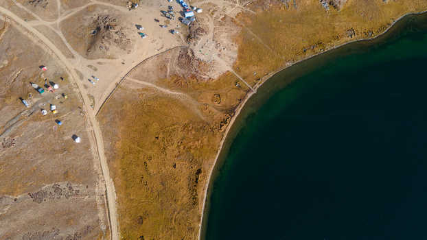 Aerial view of the shoreline of Sheosar Lake with dry grassy terrain dirt tracks and small campsites in Skardu Gilgit Pakistan.