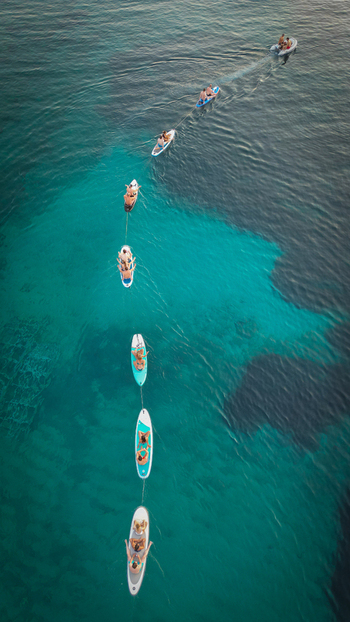 Hvar Croatia 21 August 2023 Aerial view of people on stand up paddleboards and a small boat in a line across the turquoise waters of Vinogradisce bay. Hvar Croatia 21 August 2023 Aerial view of people on stand up paddleboards and a small boat in a line across the turquoise waters of Vinogradisce bay.