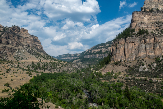 Aerial view of the rugged Shoshone River canyon featuring towering rock cliffs lush green vegetation and a winding road under a blue sky in Cody Wyoming United States. Aerial view of the rugged Shoshone River canyon featuring towering rock cliffs lush green vegetation and a winding road under a blue sky in Cody Wyoming United States.
