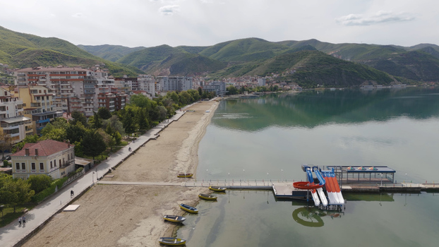 Aerial view of the lakefront with a sandy beach a pier featuring water slides and mountains in the background in Pogradec Korce County Albania. Aerial view of the lakefront with a sandy beach a pier featuring water slides and mountains in the background in Pogradec Korce County Albania.
