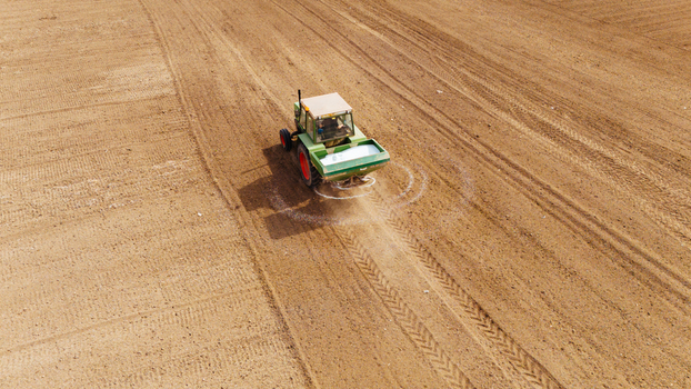 Aerial view of a tractor spreading fertilizer over a field casting a shadow on the dry furrowed earth Sremska Mitrovica Vojvodina Serbia. Aerial view of a tractor spreading fertilizer over a field casting a shadow on the dry furrowed earth Sremska Mitrovica Vojvodina Serbia.