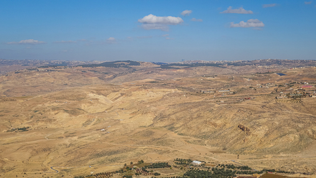 View of the arid landscape and rolling hills surrounding Wadi Musa featuring rocky terrain sparse vegetation and a clear blue sky in Wadi Musa Ma an Governorate Jordan. View of the arid landscape and rolling hills surrounding Wadi Musa featuring rocky terrain sparse vegetation and a clear blue sky in Wadi Musa Ma an Governorate Jordan.